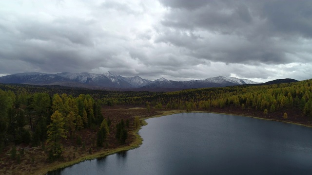 美丽明亮的森林在地平线雪山石峰。高全景飞无人在农村植物。旅游目的地田园风光。傍晚烟雾戏剧性的天空和宁静的池塘宽拍摄视频素材