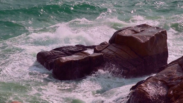 巨大的海浪拍打着岩石峭壁，溅起白色的泡沫。用波浪拍打着海岸的石头。4K和特写视频素材