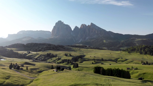 在意大利多洛米特(Dolomites)的Suisi阿尔卑斯(Alpe di Suisi)，向后飞过盛开的田野，草地上有传统的木屋视频素材