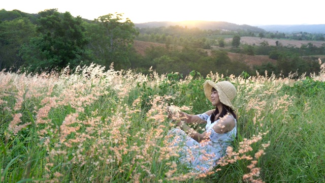 美丽的女子坐在山上的草地上，夕阳西下，带着放松和浪漫的心情。视频素材