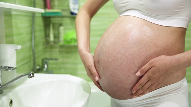 怀孕的女孩在浴室里用乳霜润滑胃来防止妊娠纹视频素材