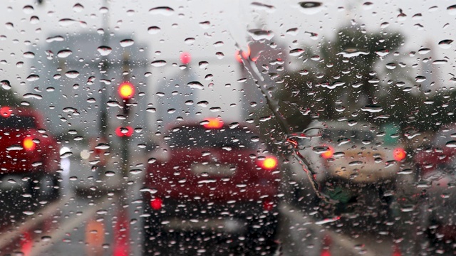 雨落在汽车挡风玻璃上。在暴雨暴雨中驾驶汽车行驶在交通堵塞的街道上，车内一辆汽车行驶着，模糊了交通灯的背景。视频素材