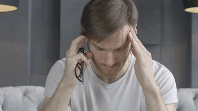 特写:疲倦的白人男子摘下眼镜，揉搓太阳穴。英俊疲惫的黑发男人有压力。头痛，紧张性疼痛，工作过度。电影4k ProRes总部。视频素材