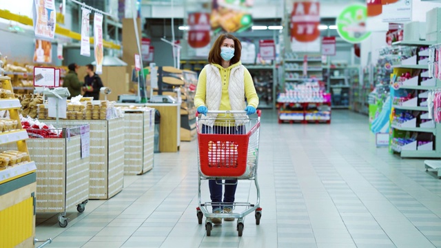 家庭主妇戴着医用口罩和手套，推着手推车在超市购物视频素材