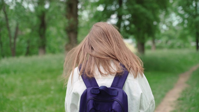 美丽的女人微笑着走在被树叶和树木包围的小路上。后视图的女性与背包行走在夏季公园视频素材