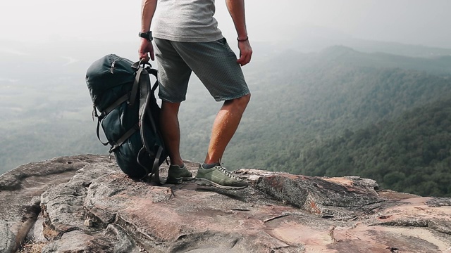 山谷风景的背包客。一个徒步旅行者拿着背包和树叶站在山的边缘视频素材