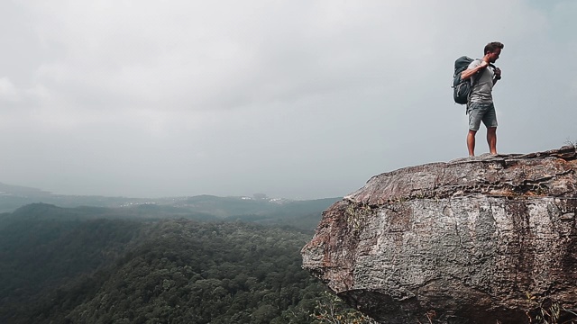 山谷风景的背包客。一个徒步旅行者坐在山的边缘，然后背着背包和树叶视频素材