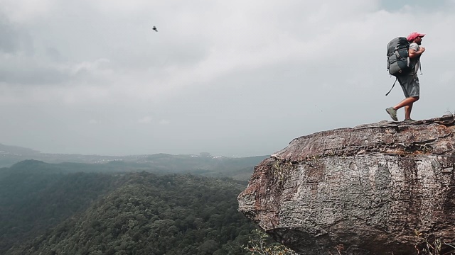 山谷风景的背包客。一个徒步旅行者背着背包站在山的边缘，背着树叶视频素材