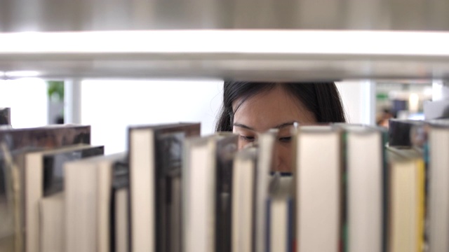 亚洲女学生在图书馆的书架上找到一本书视频素材