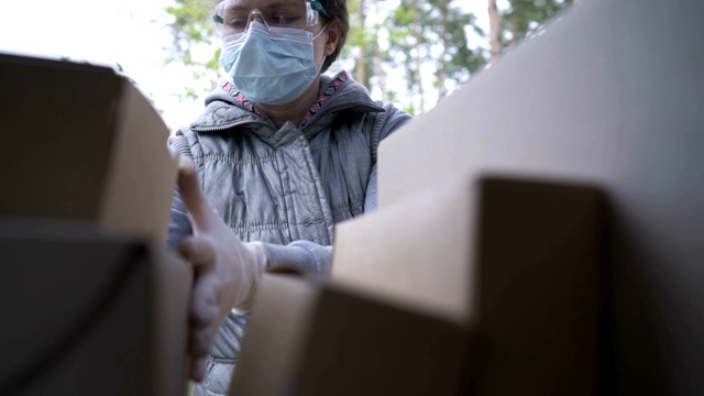 一名身穿防护服的志愿者将箱子装进汽车后备箱。在冠状病毒大流行期间，为在家工作和保持社交距离提供食品配送服务。网上购物。视频素材