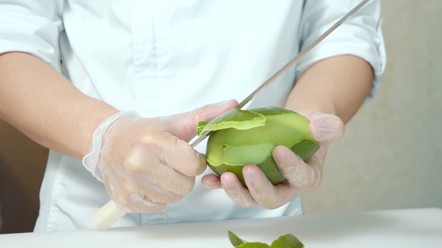 男性手的特写，一个厨师在手套从牛油果皮与刀在厨房。健康的素食视频素材