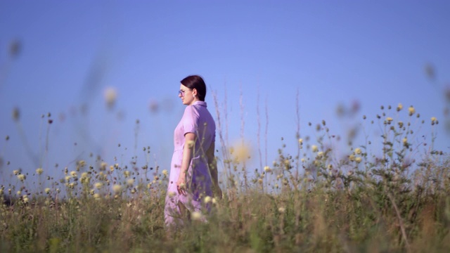 穿紫色衣服的女孩走过开着野地花的田野视频素材