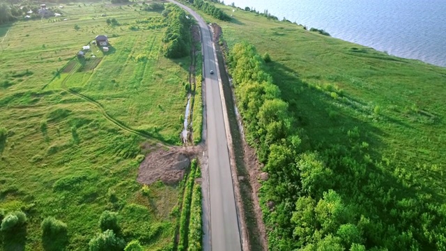 一条孤独的道路，一边是一个湖，另一边是无边无际的田野，远处是小房子和一个村庄视频素材