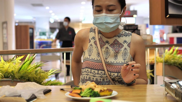 新的正常的饮食。亚洲妇女在餐厅吃午餐前摘下口罩视频素材