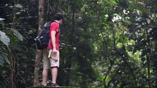 一位亚洲华人青年在丛林雨林徒步旅行路线上看地图视频素材