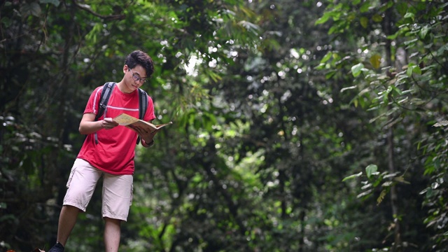 一位亚洲华人青年在丛林雨林徒步旅行路线上看地图视频素材