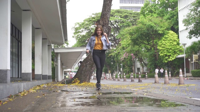 低角度的微笑年轻美丽的女人跑过水坑在雨后的人行道。快乐漂亮的少女享受和有乐趣在雨天。视频素材