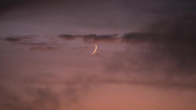 晚霞背景中的新月。月亮，在浮云中，在玫瑰色的夕阳中下沉。日落时云飘浮。视频素材