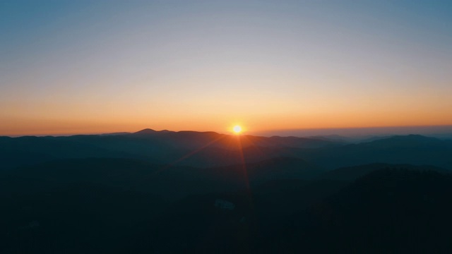 镜头光晕在山在橙色日落在夏季傍晚航拍无人机滑上来。太阳射线。青松林山坡的山脉。一轮太阳在蓝天中缓缓落山。自然视频素材