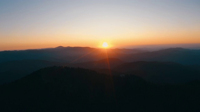 镜头光晕在山在橙色日落在夏季傍晚航拍无人机滑上来。太阳射线。青松林山坡的山脉。一轮太阳在蓝天中缓缓落山。自然视频素材