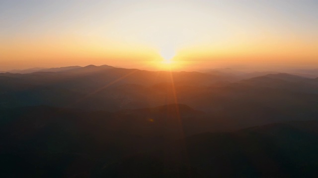 镜头光晕在山在橙色日落在夏季傍晚航拍无人机滑上来。太阳射线。青松林山坡的山脉。一轮太阳在蓝天中缓缓落山。自然视频素材