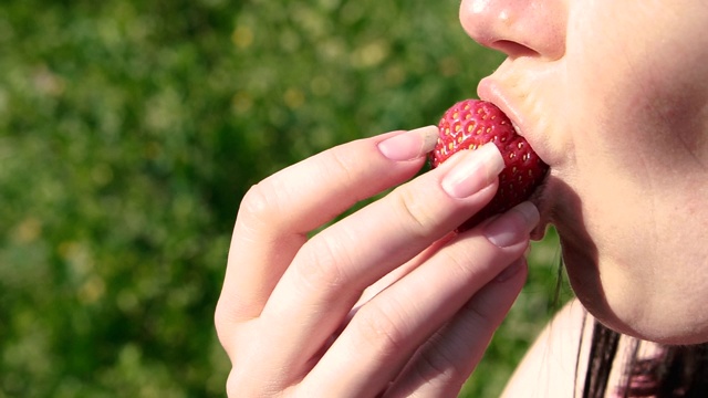 草莓。一个女人在咬一颗红草莓。视频素材