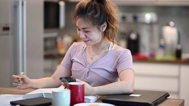 一位美丽的亚洲华裔女子在家里学习，准备她的大学考试，并查看手机短信视频素材