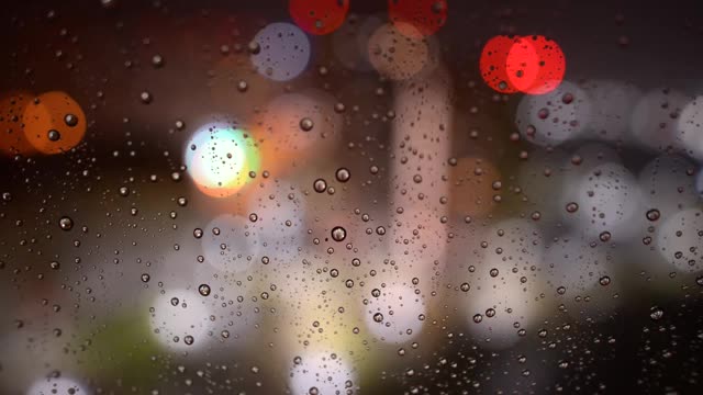 夜里雨点从玻璃上滚下来。雨点落在散景背景的玻璃上。窗外夜雨绵绵视频素材