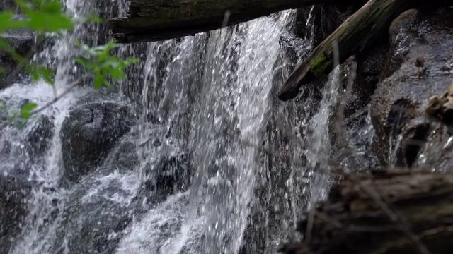 近距离拍摄瀑布顶部，树枝和原木悬在悬崖边缘，水流如瀑布般倾泻至下面的河流。视频素材