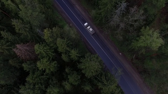 鸟瞰图的一个大拖车载着一辆破汽车沿着森林道路。视频素材