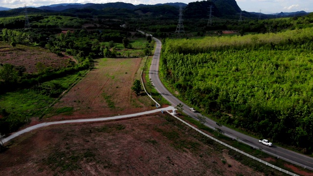 鸟瞰图的白色汽车行驶在乡村道路在森林。无人机在松树林的砾石路上飞行视频素材