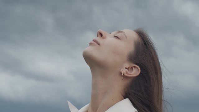 近距离的肖像女性的脸看向暴风雨的天空复制文本空间手持设备。年轻女子摆姿势的自然背景户外慢动作。信任希望爱的概念。面部护理视频素材