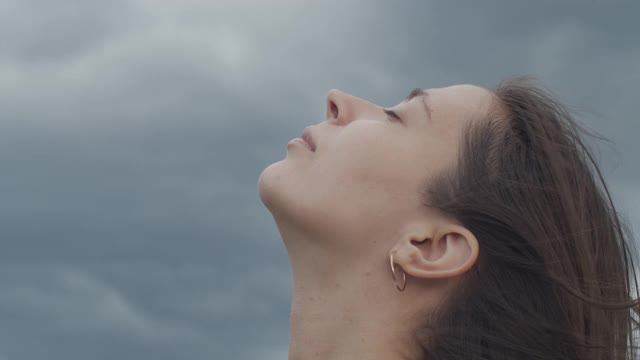 近距离的女性脸的肖像仰望暴风雨的天空复制文本空间。详细的宏观侧面的女人与闭上眼睛的自然雨背景慢动作。面部护理化妆品视频素材