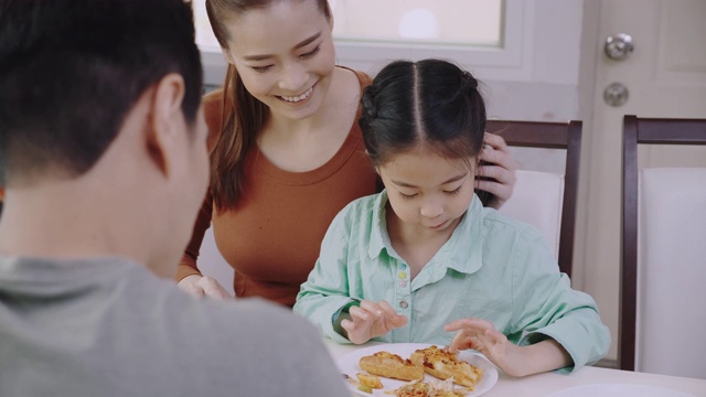 亚洲人喜欢在家吃美味的披萨。父母和女儿吃着外卖的美味意大利菜。概念食品外卖视频素材