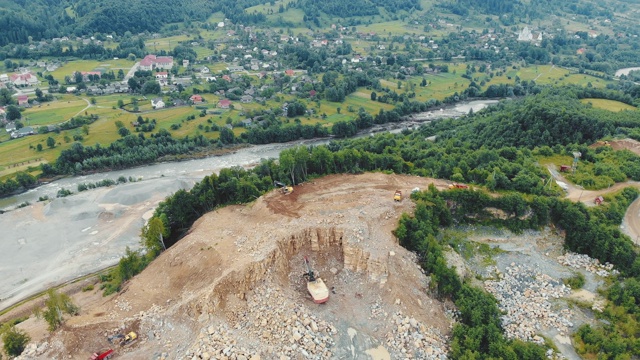 鸟瞰图飞行在一个采石场在山上开采石头和其他岩石。在一条山间河流的背景下，重型机械在采石场工作。视频素材