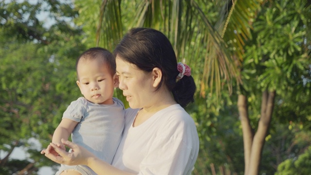 4K，妈妈抱着他的儿子在日落公园。视频素材