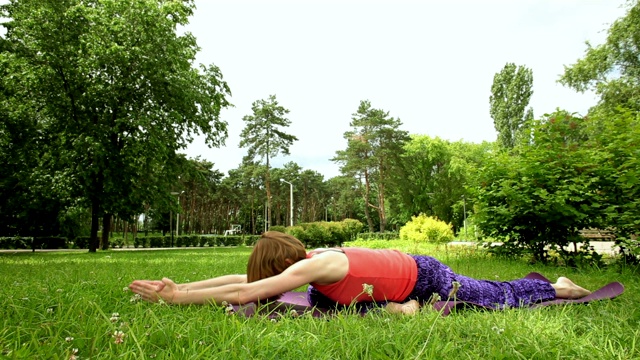 一个迷人的健康女人在夏天的一天在公园里练习瑜伽视频素材