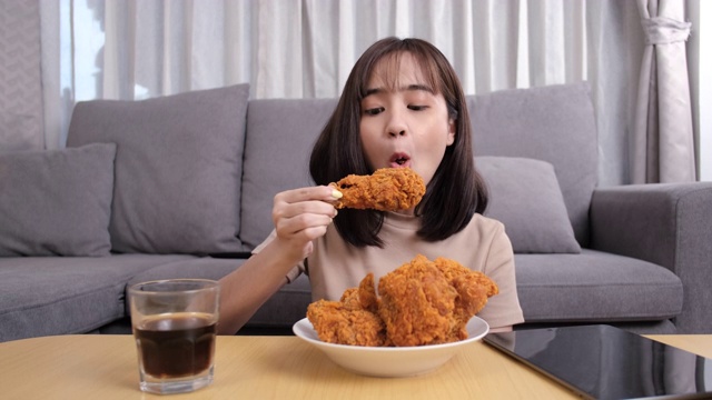 年轻的亚洲女性外卖吃垃圾食品鸡块鸡翅，女性享受快餐的乐趣，通过社交距离概念的安全和阻止冠状病毒传播的快递服务。视频素材