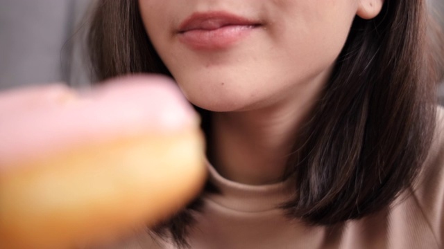 近距离观察亚洲女性外卖吃甜甜圈垃圾食品，女性在客厅享受反式脂肪，快餐配送服务安全，通过社交距离阻止冠状病毒传播。视频素材