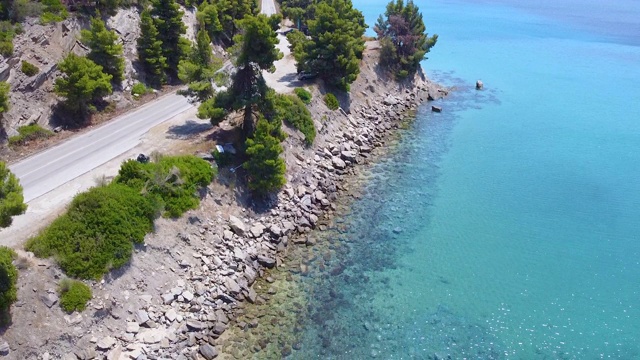 空旷的交通道路上的岩石海岸由蓝色透明的海。鸟瞰图视频素材