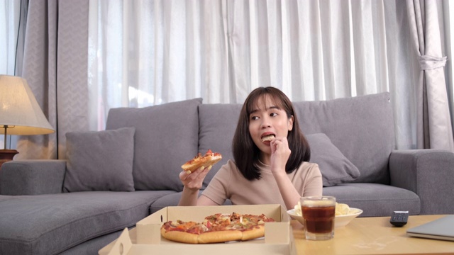 年轻的亚洲女人外卖垃圾食品吃薯条和饮料可乐在沙发上享受和看电视在家，快餐配送服务理念。视频素材