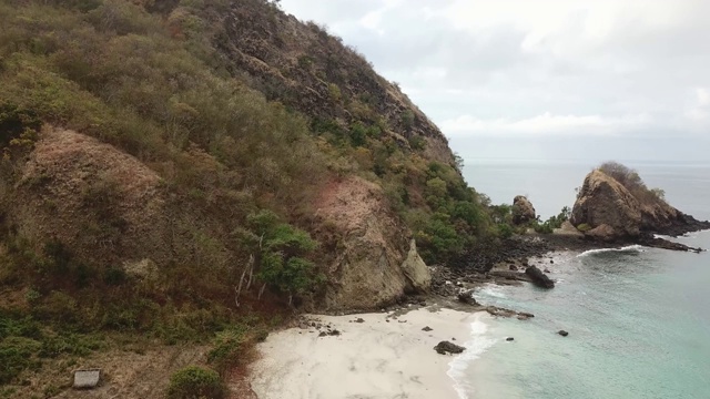 田园诗般的科卡海滩全景。印度尼西亚弗洛雷斯的隐藏宝石。海滩被海浪轻轻地冲刷着。陡峭的山丘直通大海。海上漂流的小船很少。平静和冷静视频素材