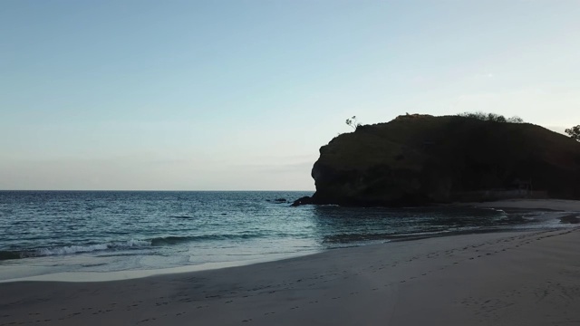 田园诗般的科卡海滩全景。印度尼西亚弗洛雷斯的隐藏宝石。海滩被海浪轻轻地冲刷着。陡峭的山丘直通大海。夕阳的柔和色彩。平静和冷静视频素材