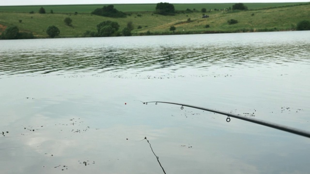 在河流或湖水中用鱼线将鱼竿拉近。湖上钓鱼。夏天河边钓鱼。在河边钓鱼视频素材