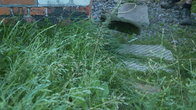 一个园丁用汽油割草机在路边割绿草。男工人在院子里割高草。人割草，草飞向不同的方向视频素材