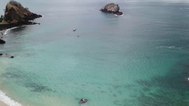 田园诗般的科卡海滩全景。印度尼西亚弗洛雷斯的隐藏宝石。海滩被海浪轻轻地冲刷着。陡峭的山丘直通大海。海上漂流的小船很少。平静和冷静视频素材