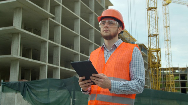 年轻建筑师或建筑工人站在工地上，用数字触控板分析方案和项目计划。视频素材