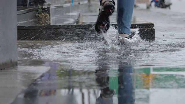 慢动作的女人跑在水坑与水溅在雨天。视频素材