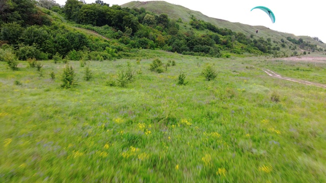 鸟瞰山上绿油油的草地，在农村人们享受滑翔伞飞行视频下载