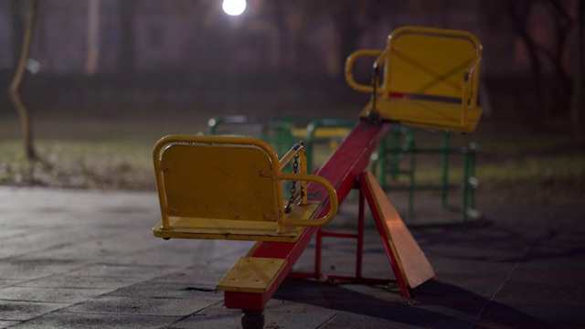 在一个秋天的夜晚，在城市公园的空旷的儿童游乐场的湿秋千。视频素材